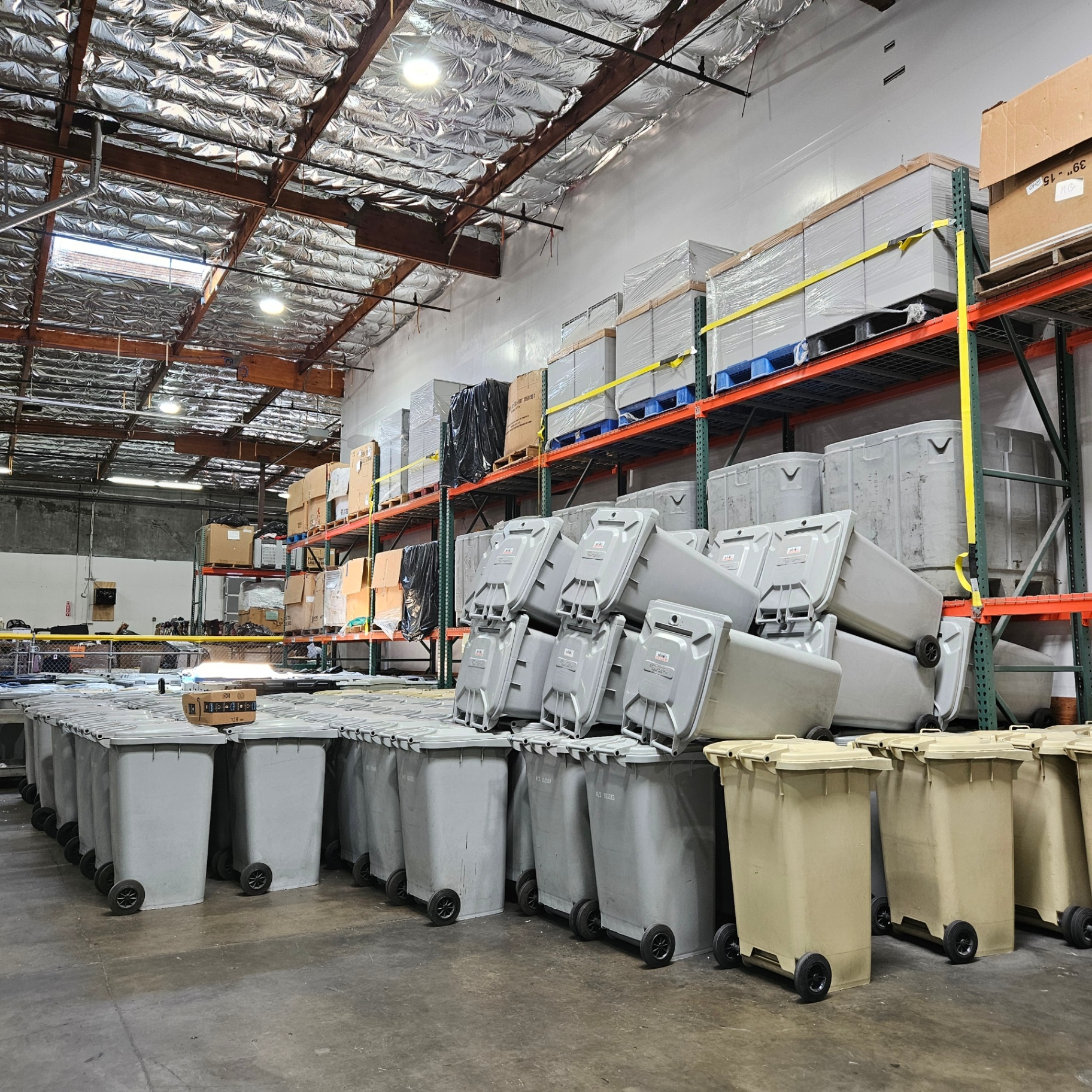 Rows of secure document collection bins staged in the UCPNB warehouse alongside pallet racking of supplies